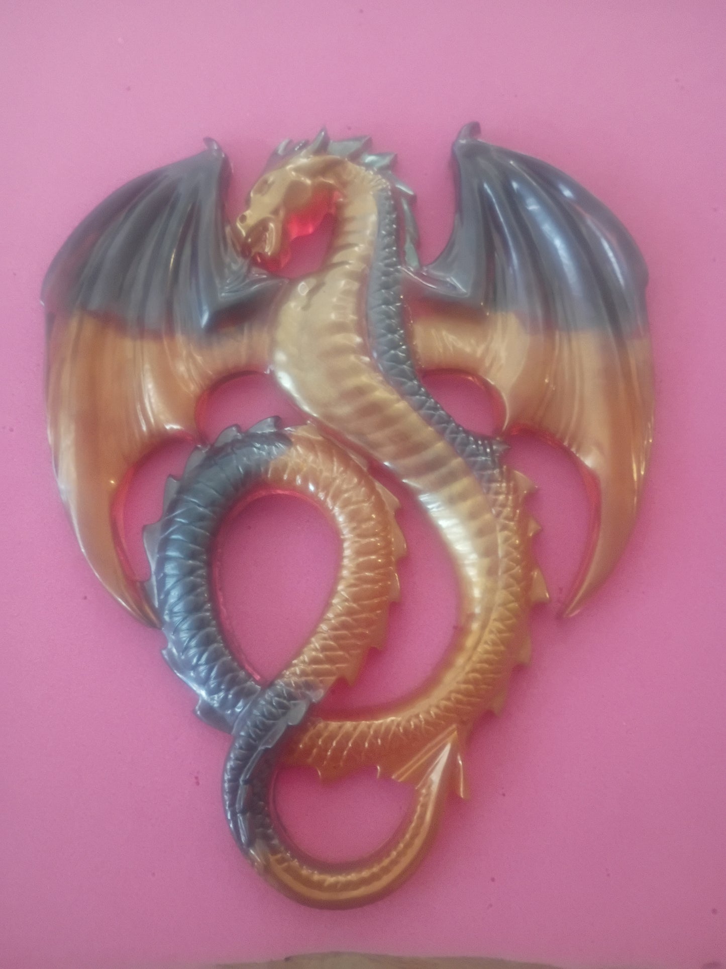 A translucent resin dragon figurine with a gold and gray color gradient, coiled in a loop against a solid pink background.